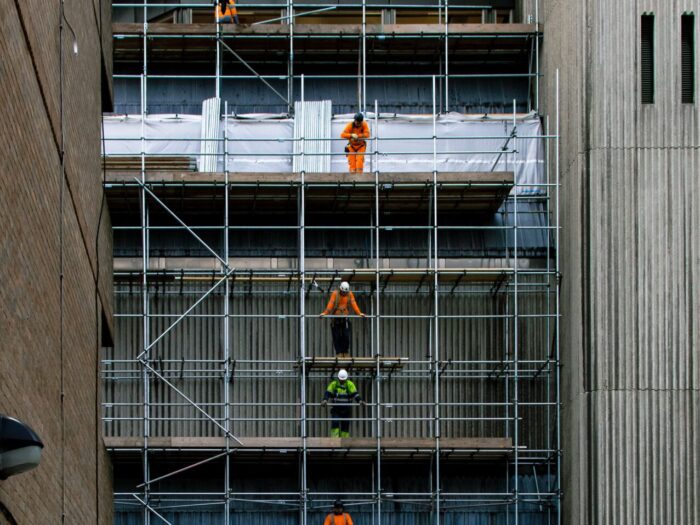 Construction workers stand on scaffolding, photograph by Chris Gray