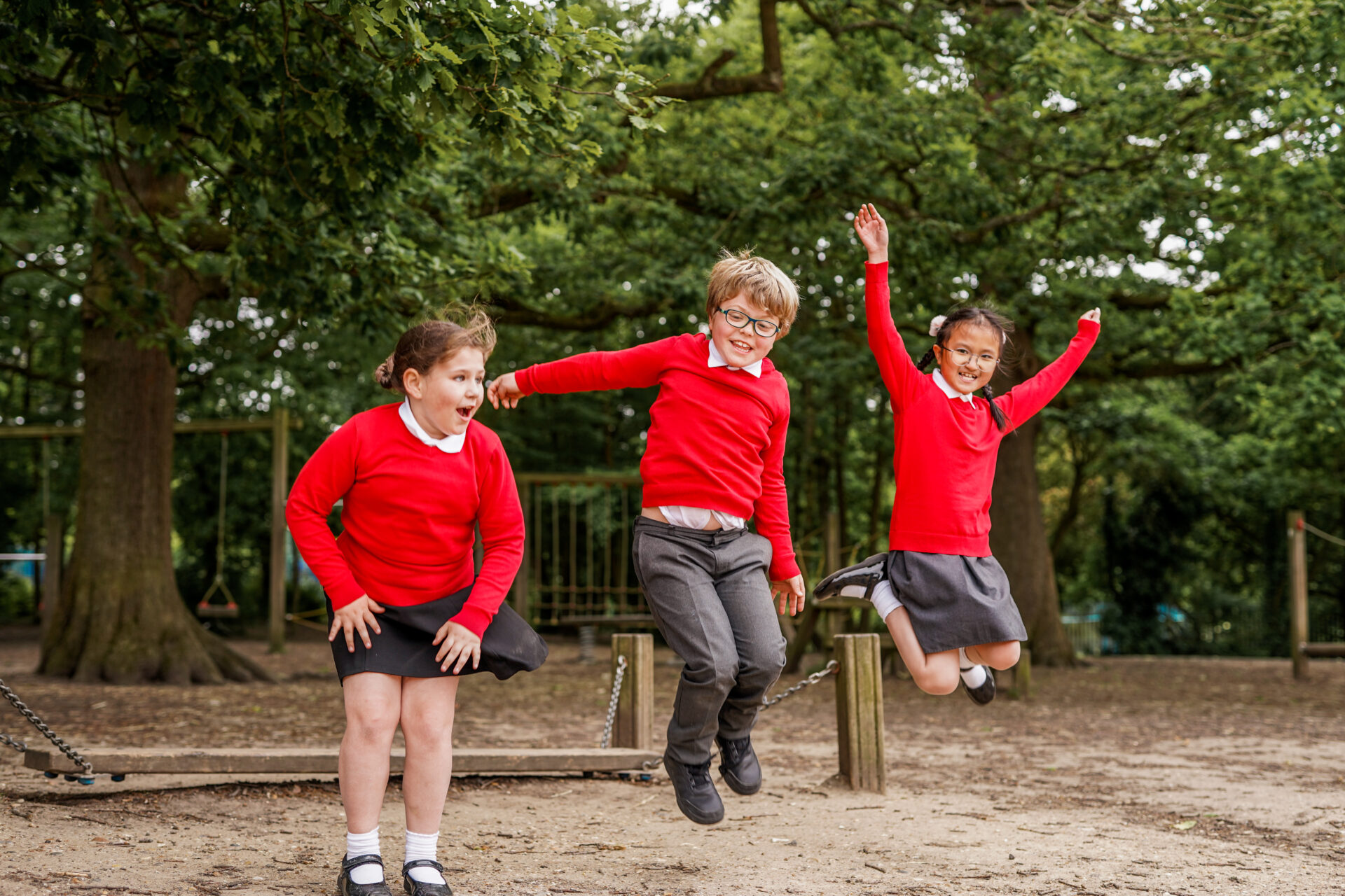 Children in red and black school uniforms jump in the air