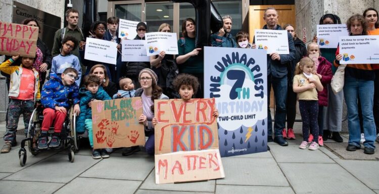 'Every kid matters'. Children sit with placards outside of the Department for Work and Pensions - photograph by Jonathan Hyams
