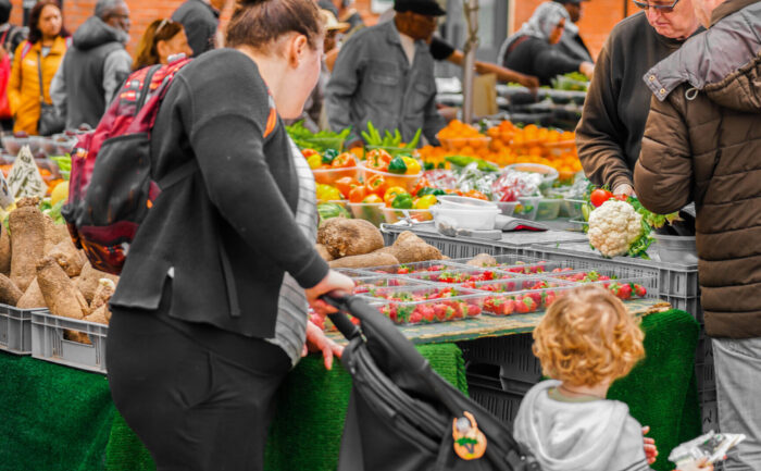 A mother and her child look at fresh produce at an outdoor market stall
