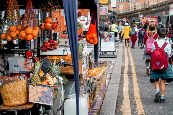 London street, with people walking past a market stall displaying fresh produce