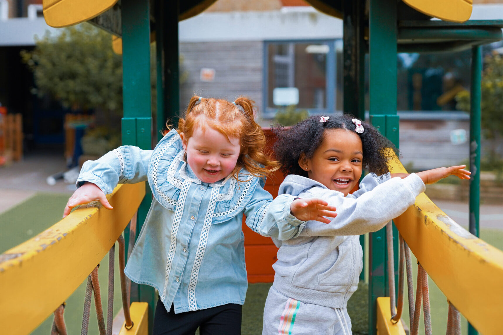 Two children laughing together, on top of a bridge in an outdoor play area.