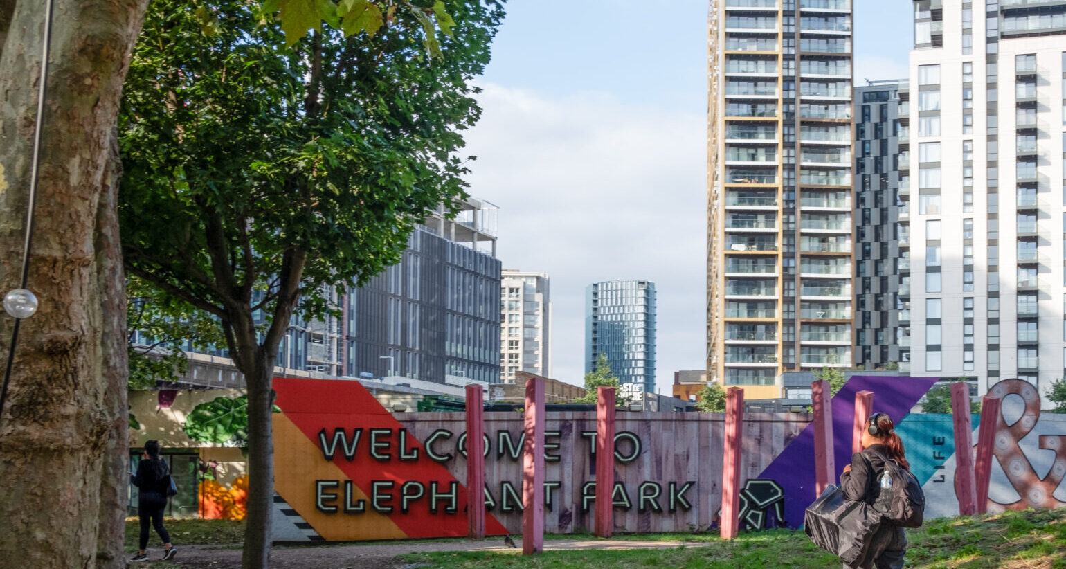 A person is walking through Elephant Park in Elephant and Castle. There is some fencing with the words 