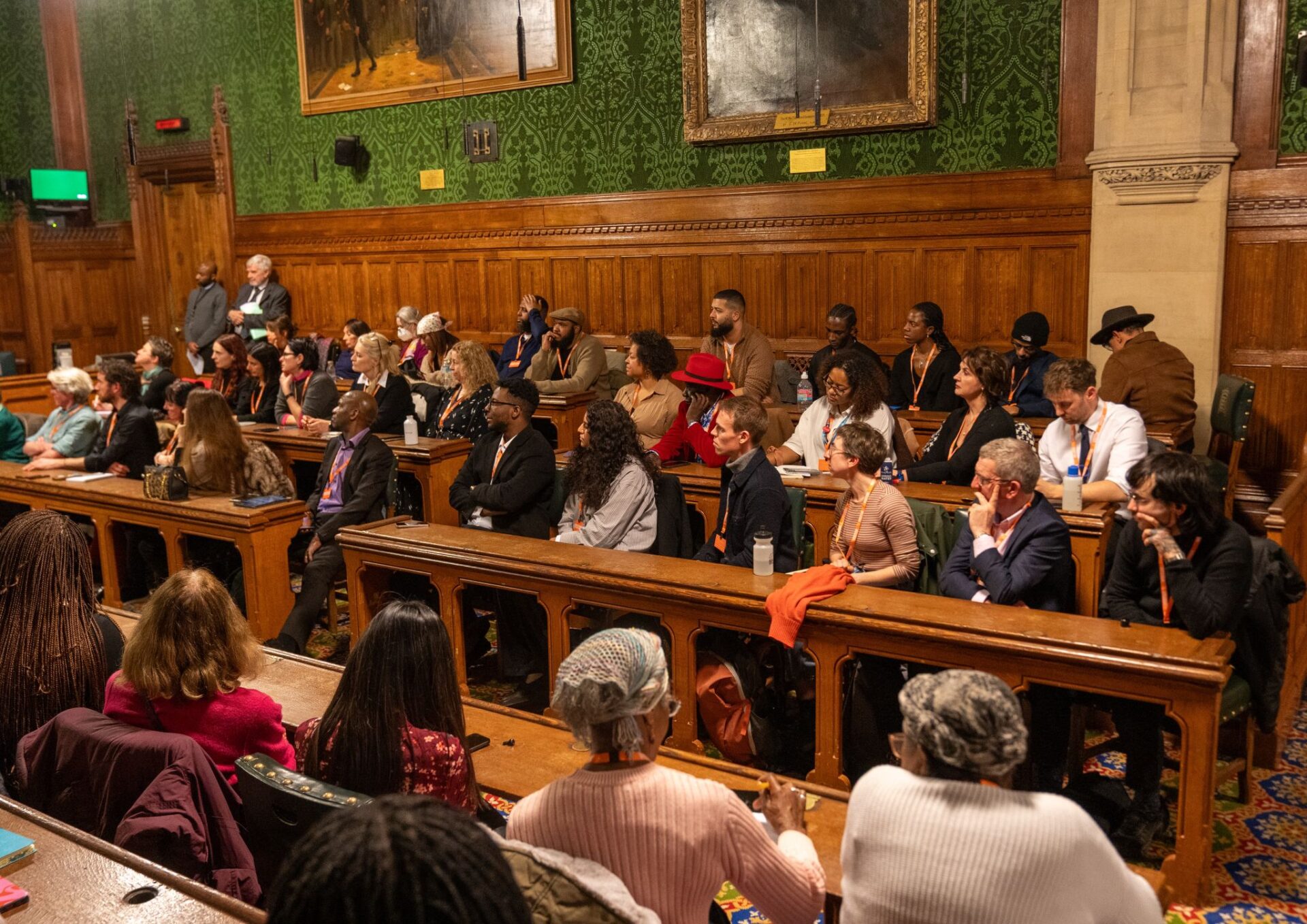 People are sitting on wooden benches and listening to a speaker at the Enact Equality event in Parliament.