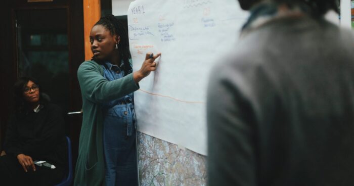 A person is pointing to a sheet of paper on a board.