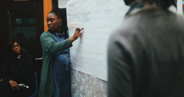 A person is pointing to a sheet of paper on a board.
