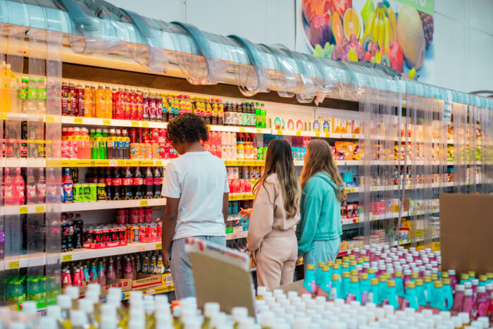 Three people are looking at drinks on display on a shop shelf
