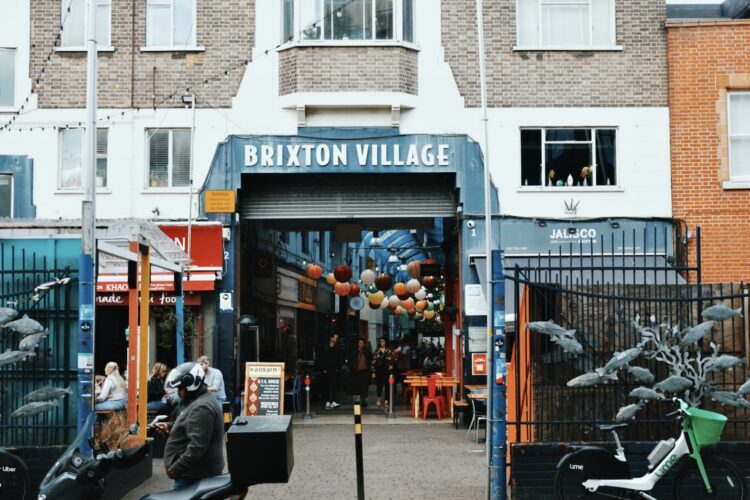 The entrance to Brixton Village. There are restaurants either side of the entrance, and people are sitting outside on tables and chairs.