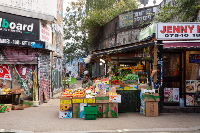 A street with shops. There are boxes of fruit and vegetables on sale.