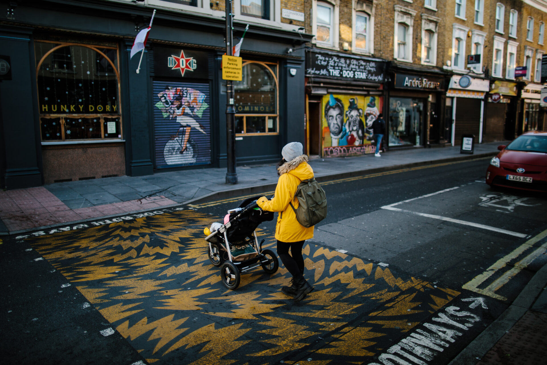 A woman is pushing a pushchair while walking across the road.