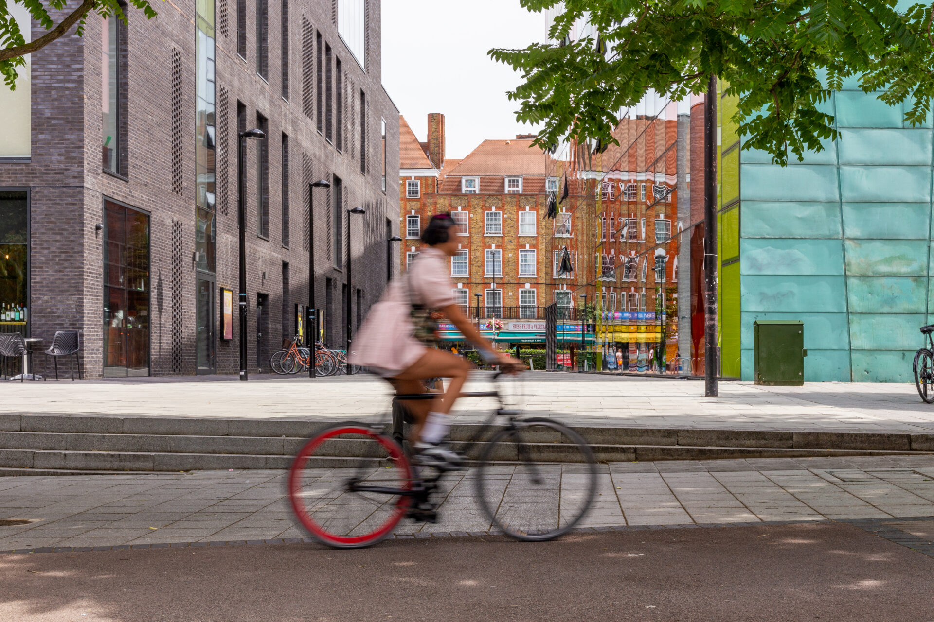 A person is cycling down a street in London. In the background are some buildings and a tree.