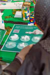 A person is looking at a sheet of paper with text: "Guess how many cubes of sugar are in each food". There are pictures of different amounts of sugar cubes.