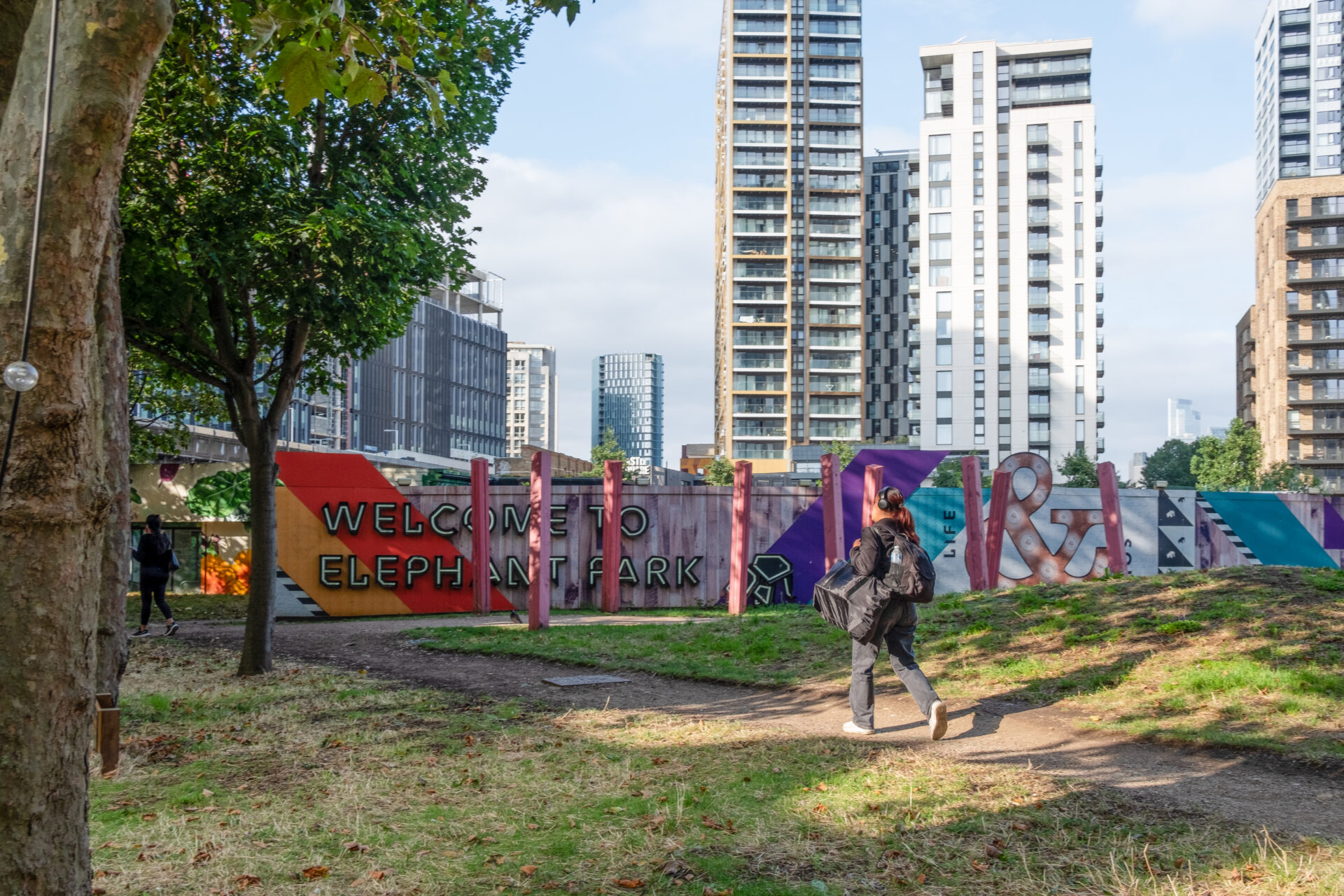 A person is walking through Elephant Park in Elephant and Castle. There is some fencing with the words 
