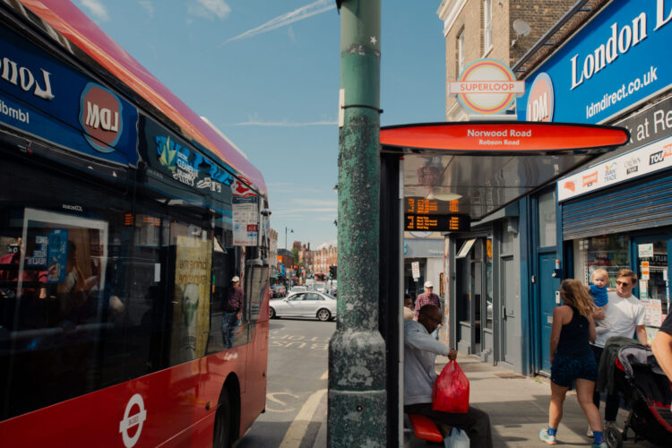 A bus next to a bus stop on the side of a street. People are waiting at the bus stop, which is called 